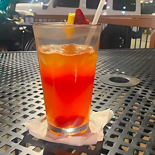 A vibrant red and orange cocktail with fruit garnish and a straw on a metal patio table.