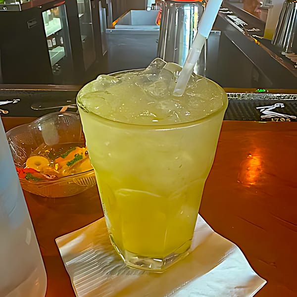 A tall glass of iced lemonade with a straw on a wooden bar counter at Trap City Cafe.