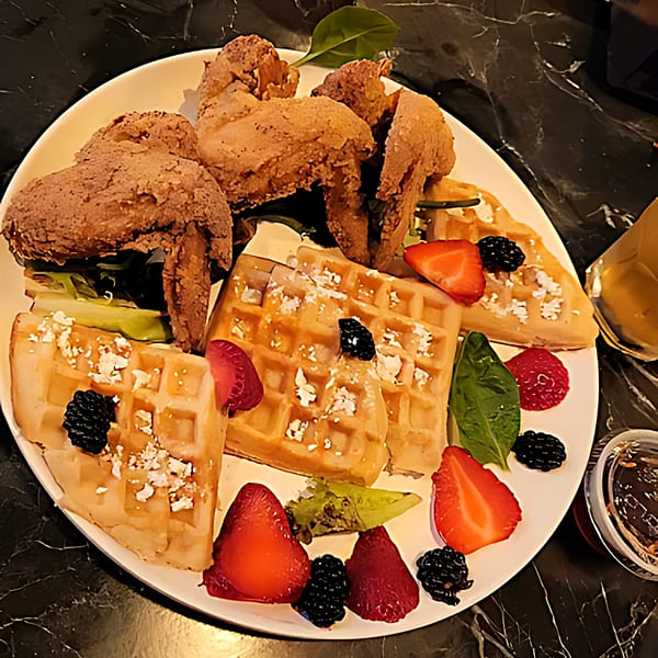 Southern fried chicken and waffles with strawberries, blackberries, and powdered sugar on a white plate.