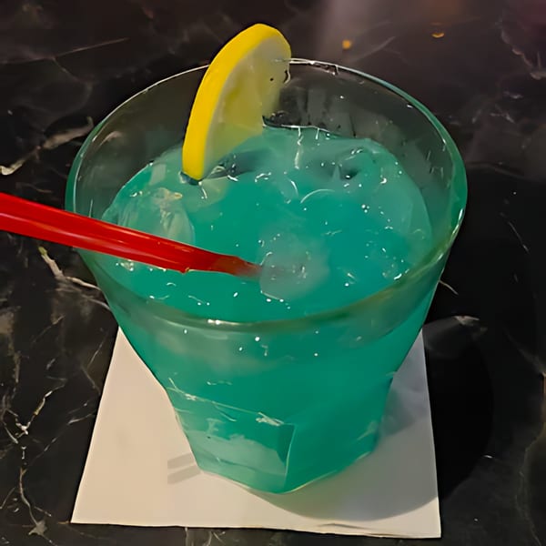 A vibrant blue cocktail with ice, a red straw, and a lemon slice on a white napkin.