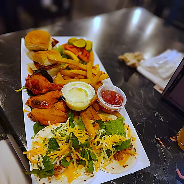 A large platter of southern food including sliders, fries, chicken wings, and tacos with sauces.